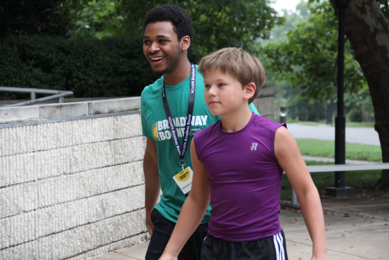 A NOVAPA Broadway Bound summer camp staff member in a camp shirt and name badge walking a young camper in to morning rehearsal in Leesburg, Virginia