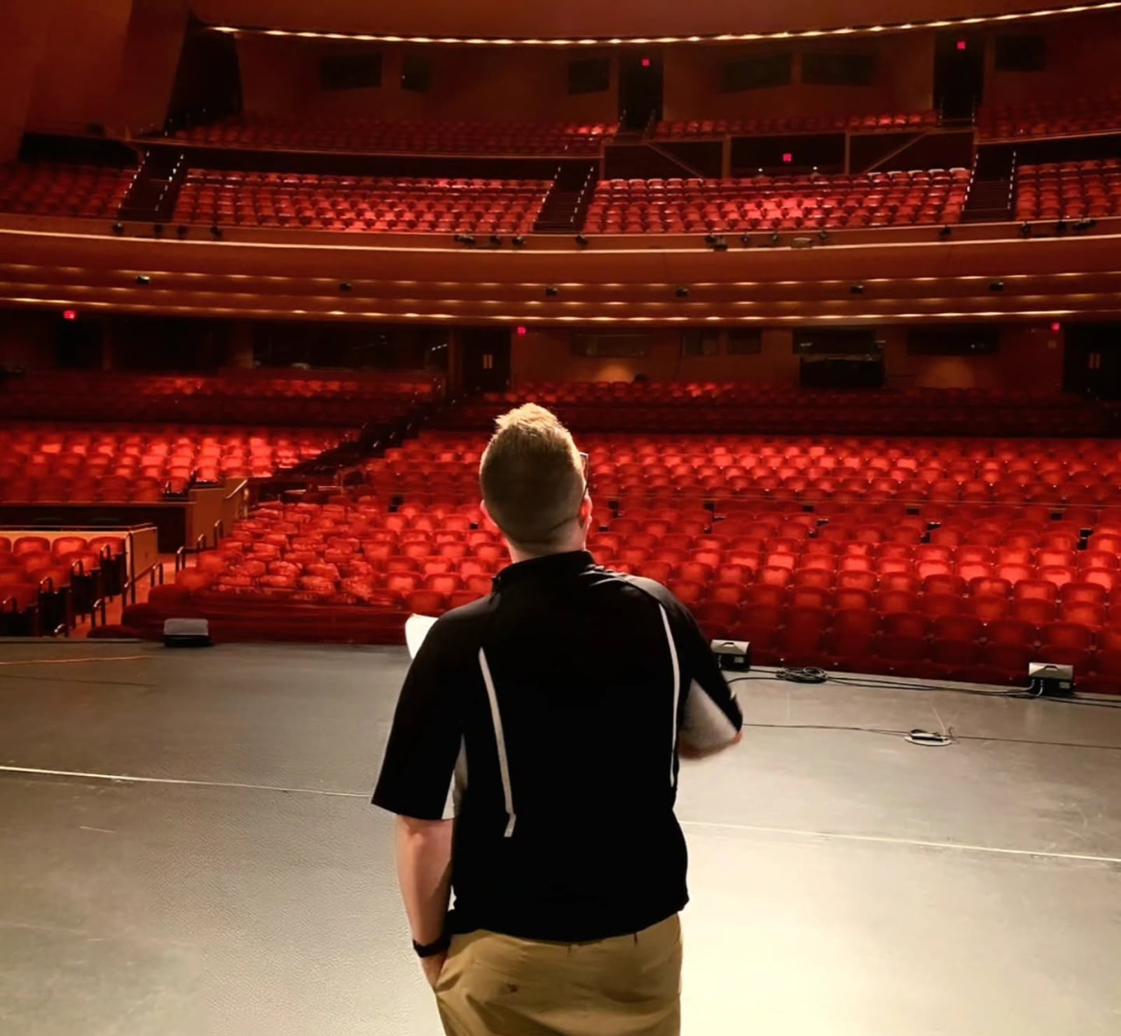 One person standing alone center stage, facing an empty theatre of red seats