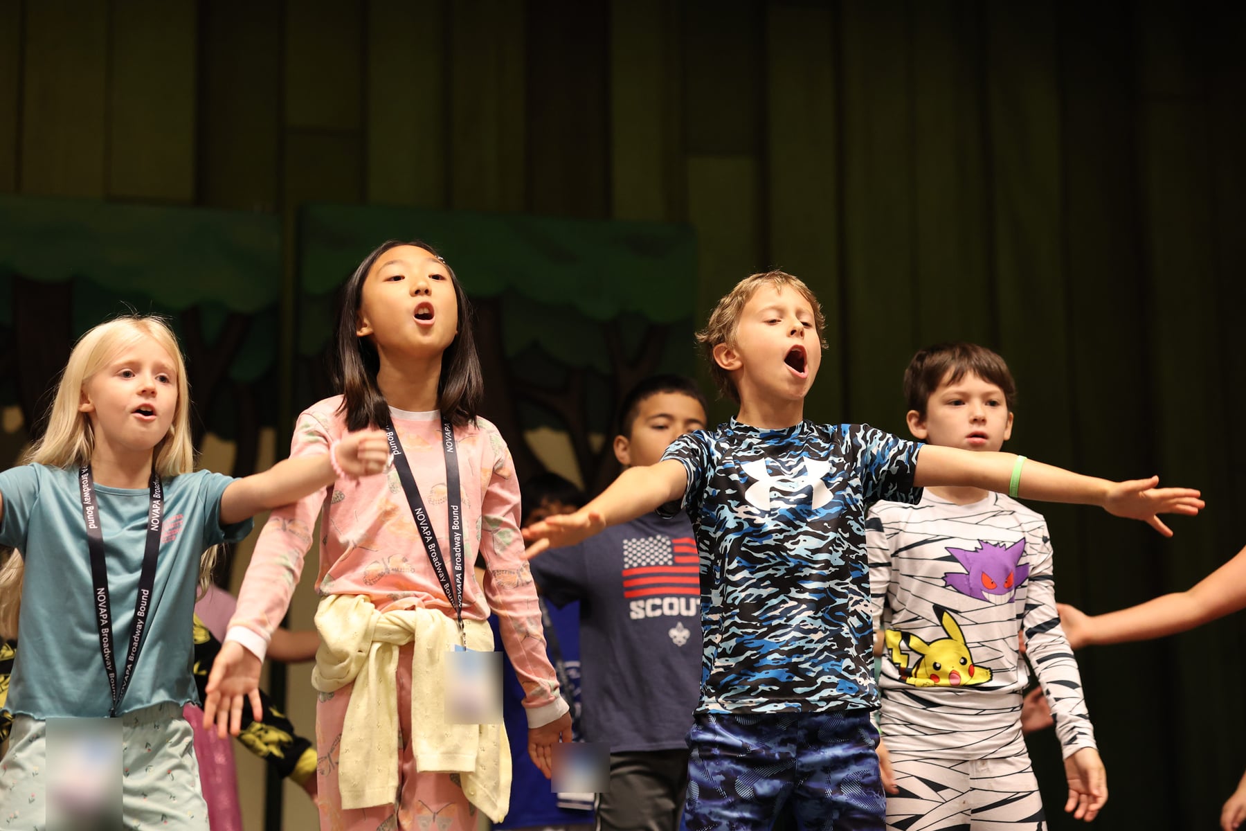 Four young performers singing together onstage with arms outstretched during a NOVAPA Broadway Bound rehearsal, none of them alone
